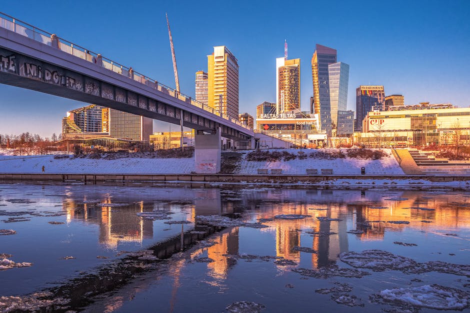 Urban cityscape with modern high-rise buildings reflecting on the river during daytime.