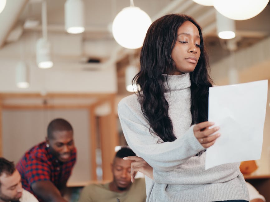 Focused woman examining a paper in a busy office setting.