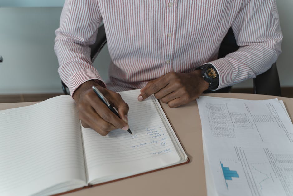Businessman in a striped shirt taking notes with documents spread on a desk, highlighting workspace focus.