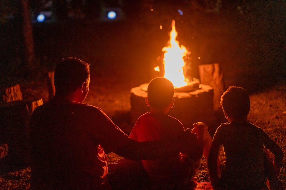 A father and two children enjoy a warm campfire together in the evening outdoors.