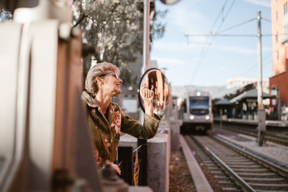 Senior woman making a fist at a train station with an urban train arriving, capturing a moment of lively expression.