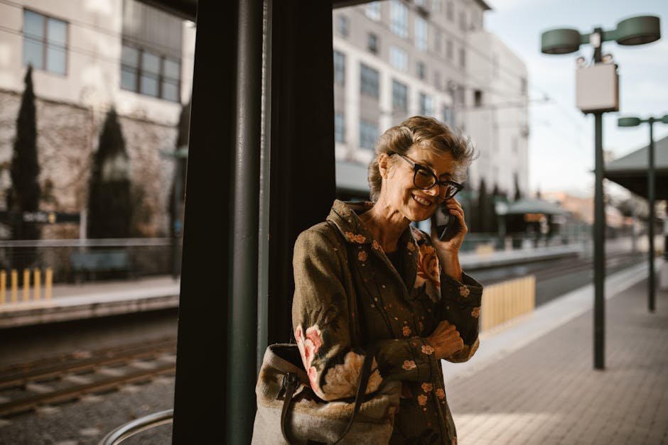 Senior woman talking on the phone, smiling at a train station platform.