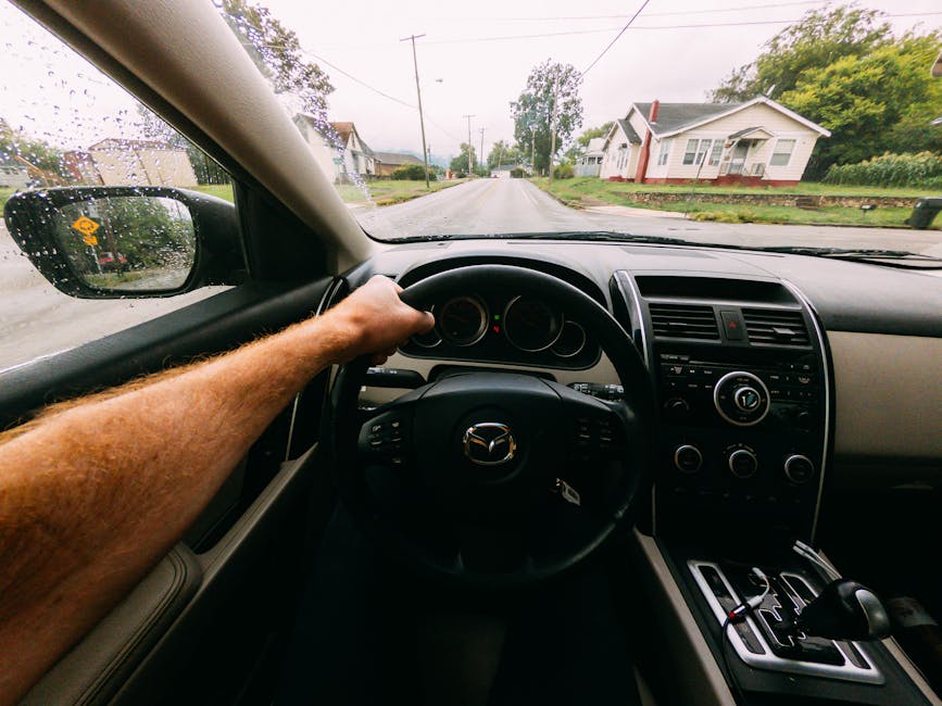 View from inside a car driving on a rainy street, showcasing the car's interior and steering control.