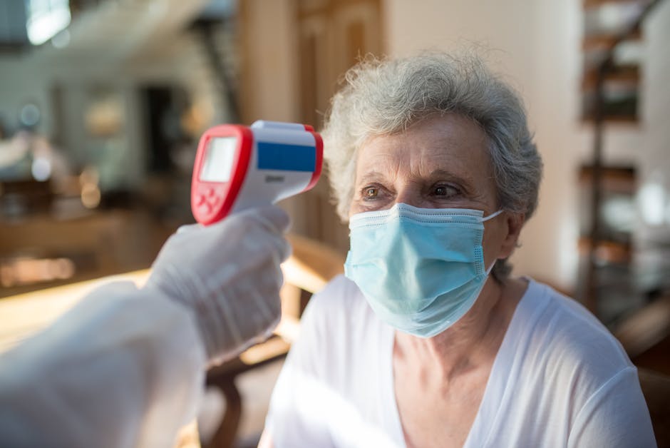 A senior woman wearing a mask receives a temperature check with an infrared thermometer indoors.