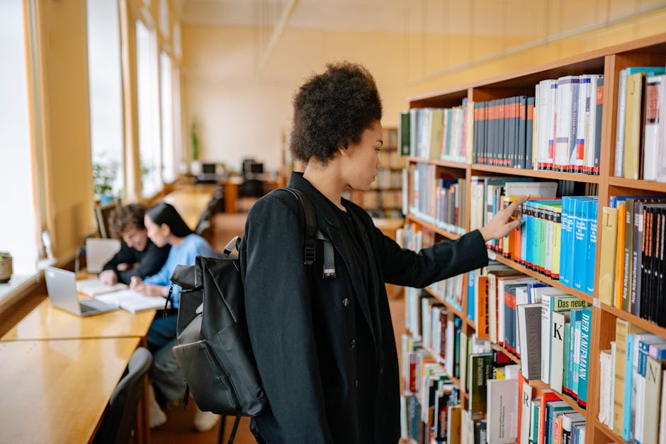 Focused student with a backpack selecting a book in a university library.