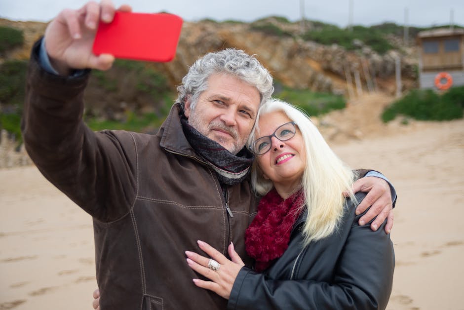 Happy senior couple embracing and taking a selfie on a beach, capturing a joyful moment.