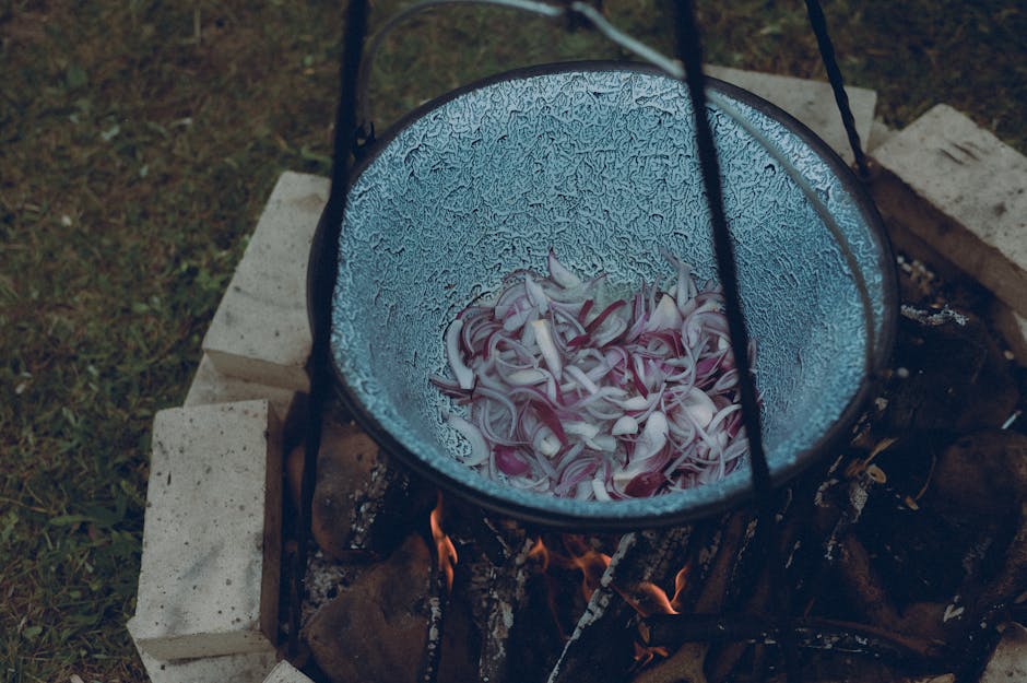 Sliced onions in a pot over an outdoor firepit, creating a rustic cooking scene.