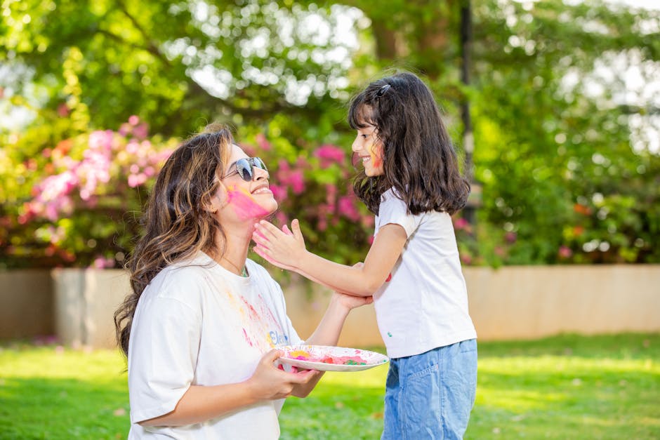 Joyful Holi celebration with mom and daughter covered in colorful powders outdoors.