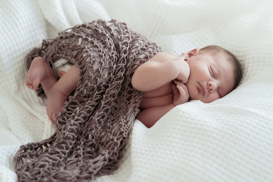 Adorable newborn baby peacefully sleeping under a knitted blanket, showcasing innocence and serenity.