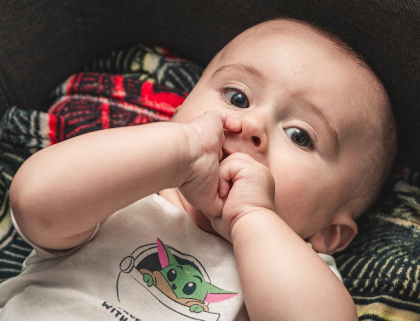 Cute baby in a onesie nibbling fingers, capturing innocence and playfulness.