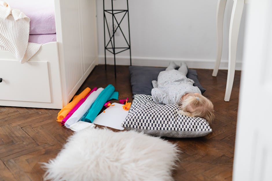 A young child naps peacefully indoors on cushions beside colorful fabric rolls.