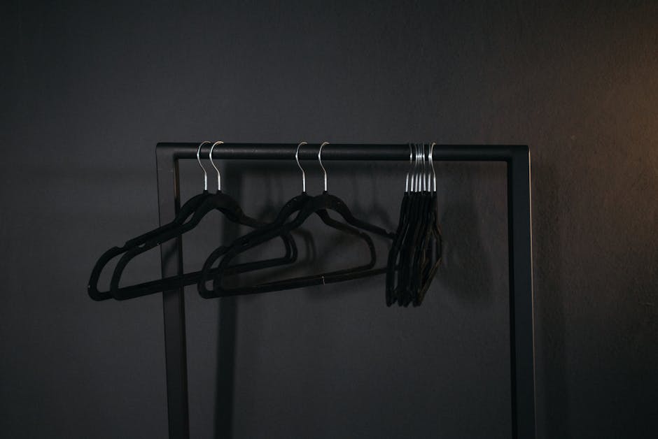 A minimalist design featuring black clothes hangers arranged on a metal rack against a dark backdrop.