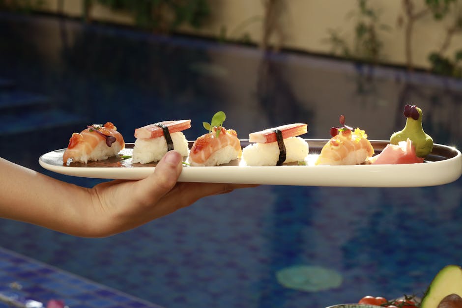 A hand presenting a meticulously prepared sushi platter in an outdoor setting by the pool.