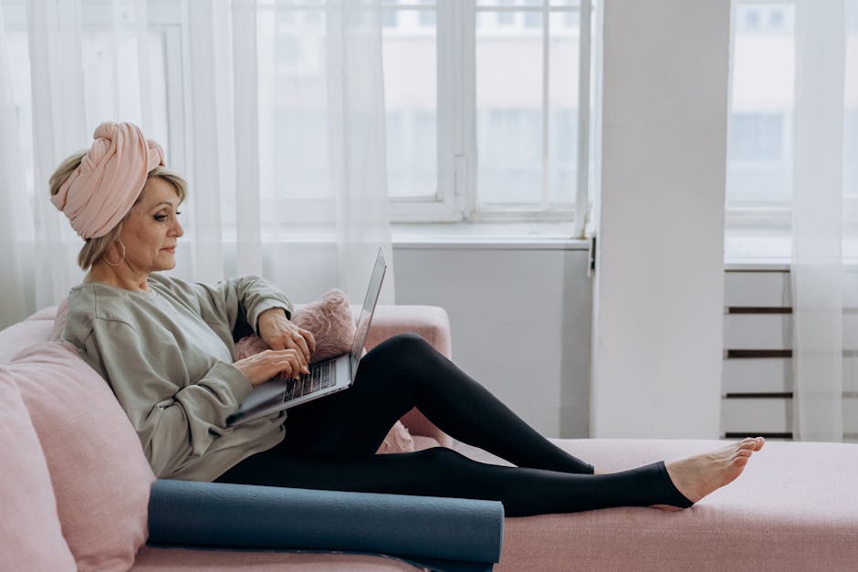 Elderly woman sitting comfortably on a sofa using a laptop indoors.