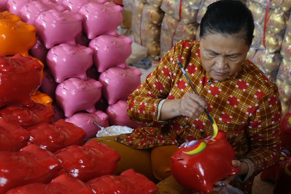 An artisan meticulously painting a red piggy bank surrounded by colorful stacks.