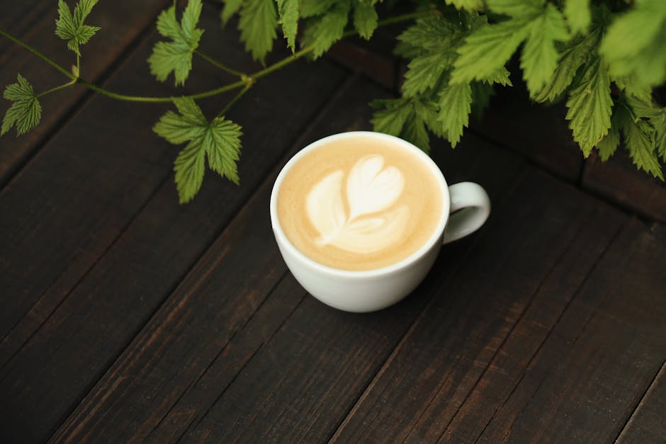 A cup of latte art coffee on a rustic wooden table with fresh green leaves, creating a serene ambiance.