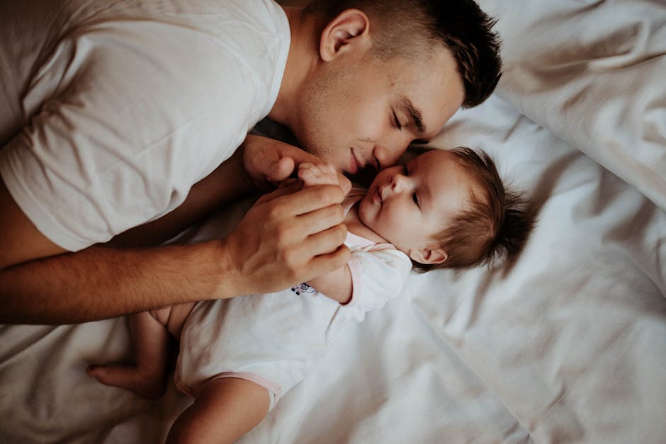 A tender moment of a father bonding with his newborn baby, lying on a bed.