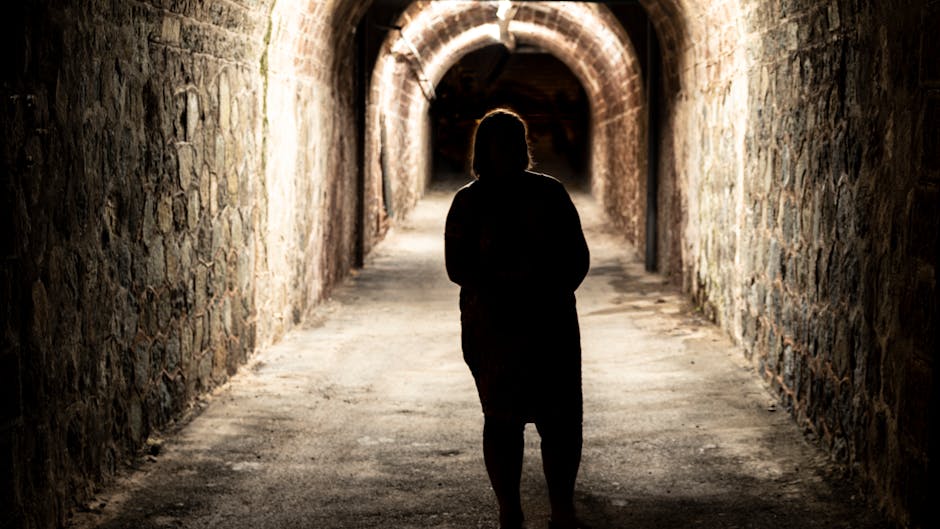 Moody silhouette of a person walking through an illuminated stone tunnel.