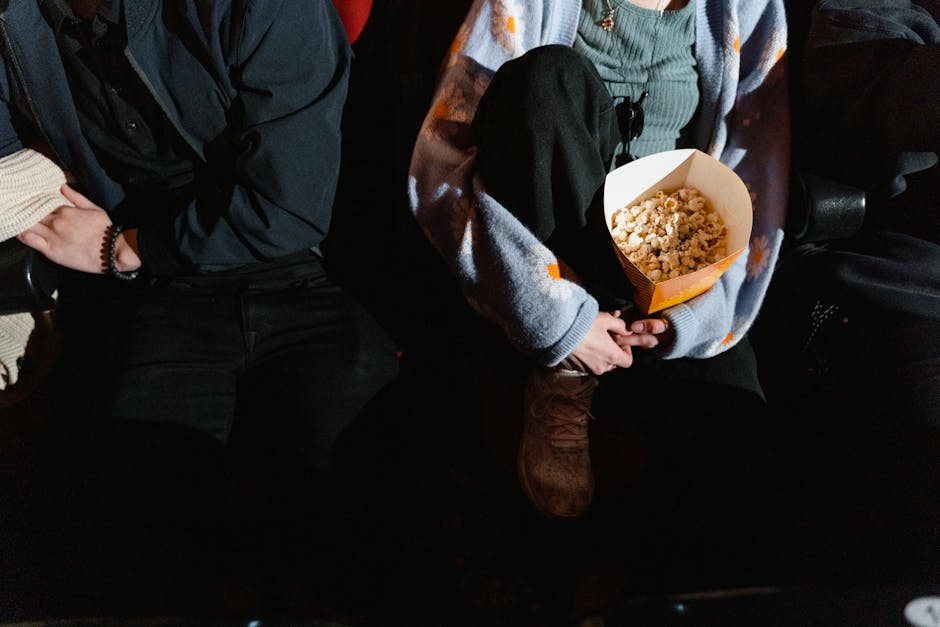 A couple sitting indoors at a movie theater, sharing a box of popcorn.