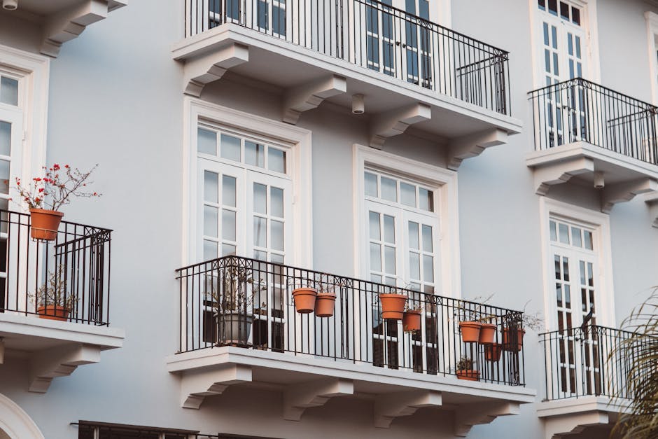 Front view of a modern building with balconies, pots, and white framed windows.