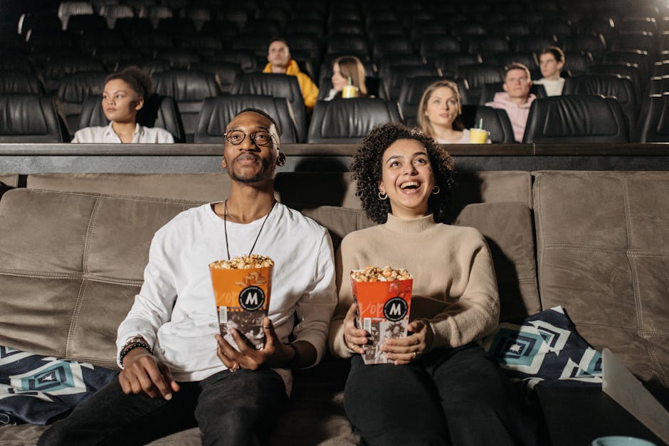 A cheerful couple watching a movie in a cinema, sharing a fun moment with popcorn.
