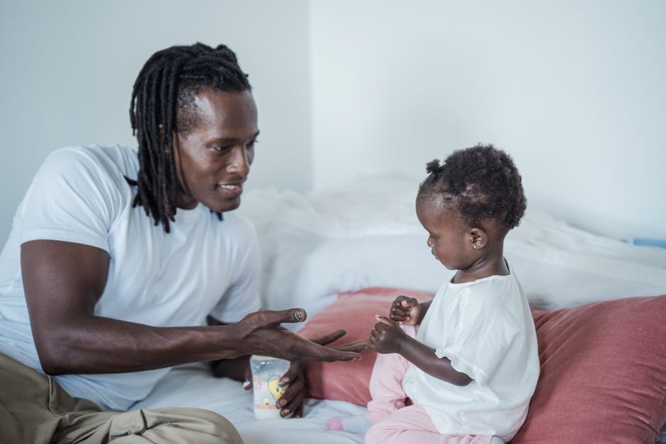 Father and young child sharing a playful moment on the bed, both wearing white shirts.