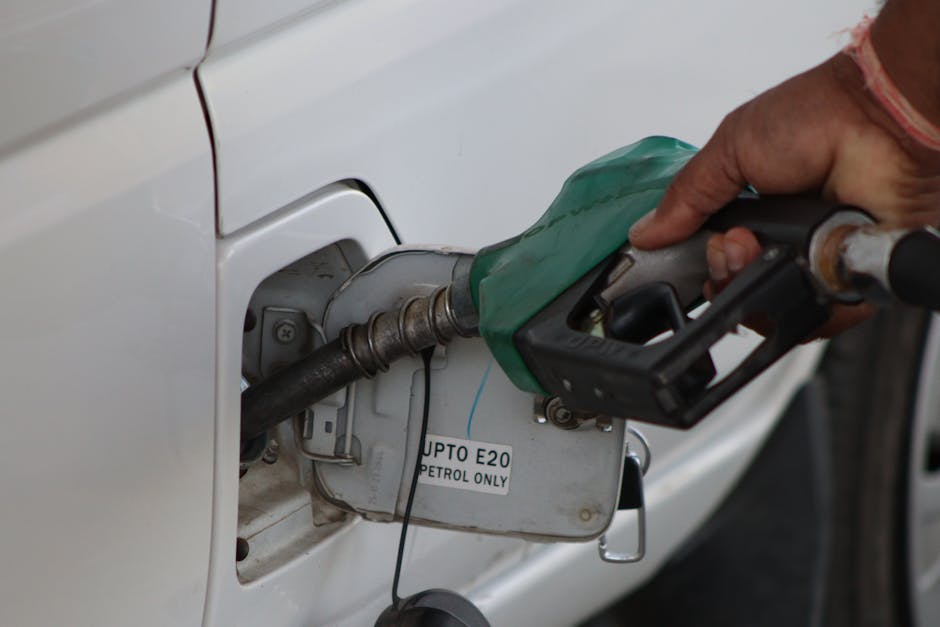 Hand refueling car with E20 petrol at a gas station, close-up view.