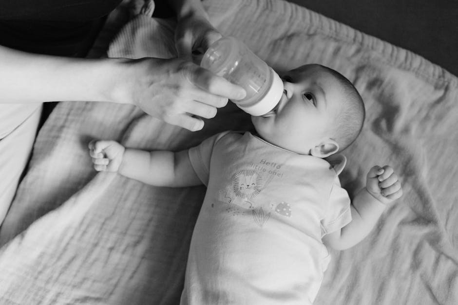 A baby being bottle-fed by a parent in a black and white photo.