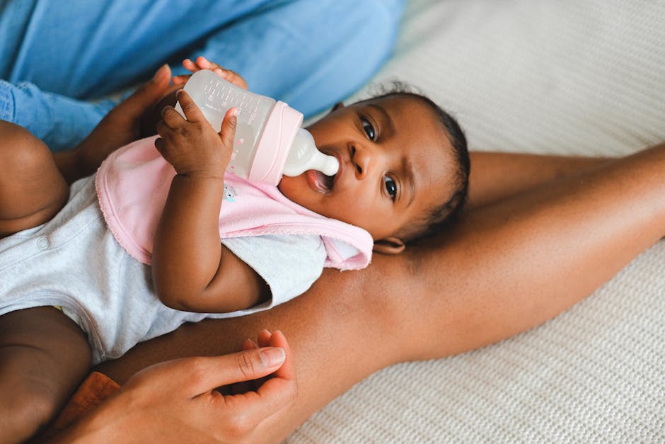 Cute baby lying down, drinking milk from a bottle, wearing a bib in a loving home environment.