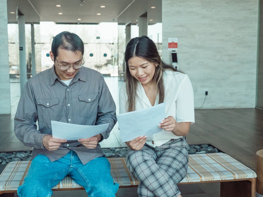 Two colleagues reading documents together on a bench in a modern office setting.