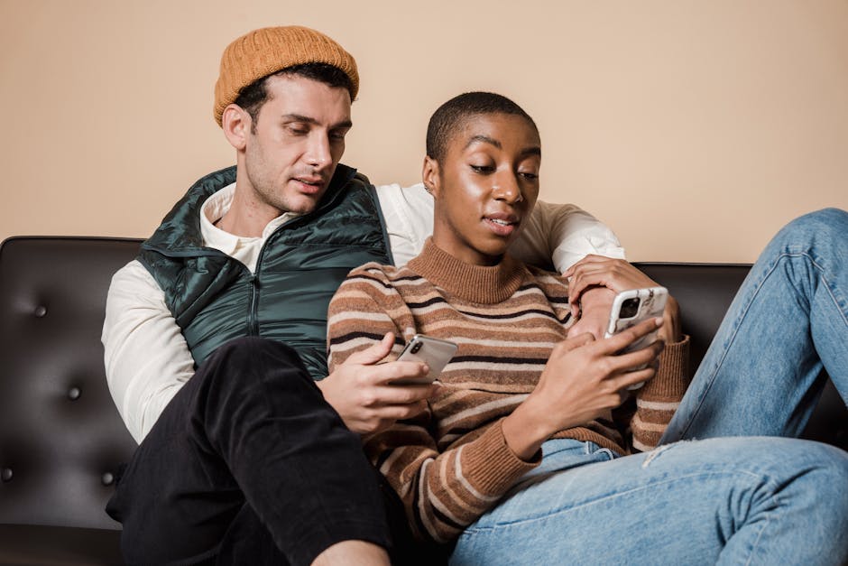 Concentrated multiracial loving couple surfing internet on cellphones while hugging on sofa in living room while spending time together at home