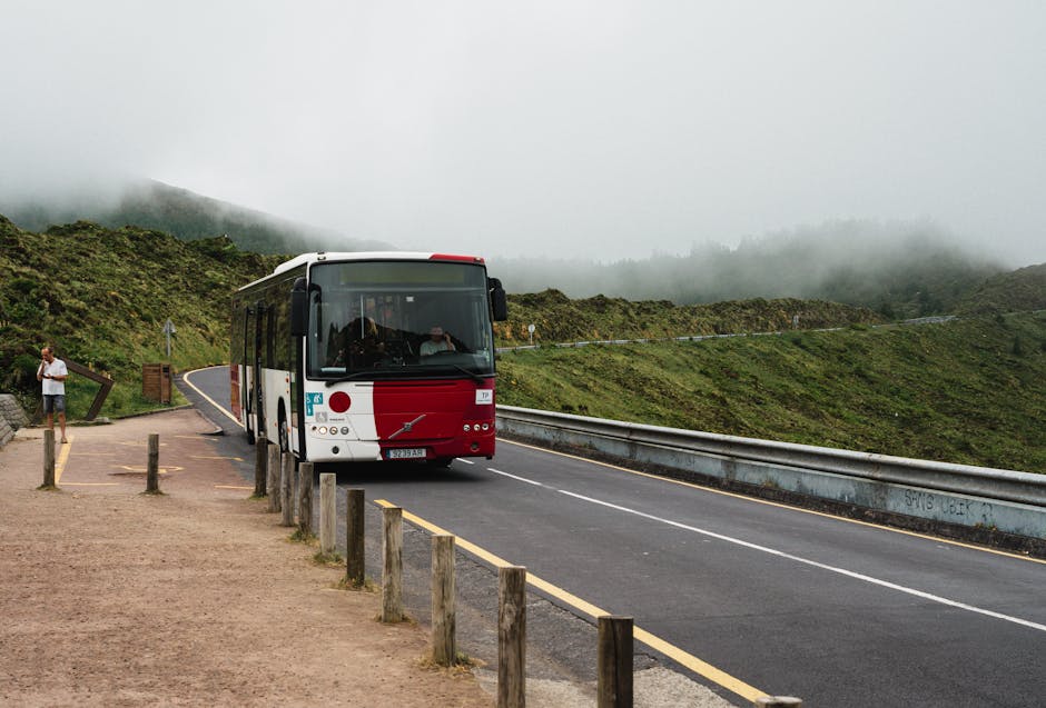 A bus navigates a foggy rural road in Azões, Portugal, surrounded by lush greenery.