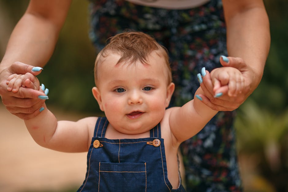A cute baby guided by an adult as they take their first steps outside on a sunny day.