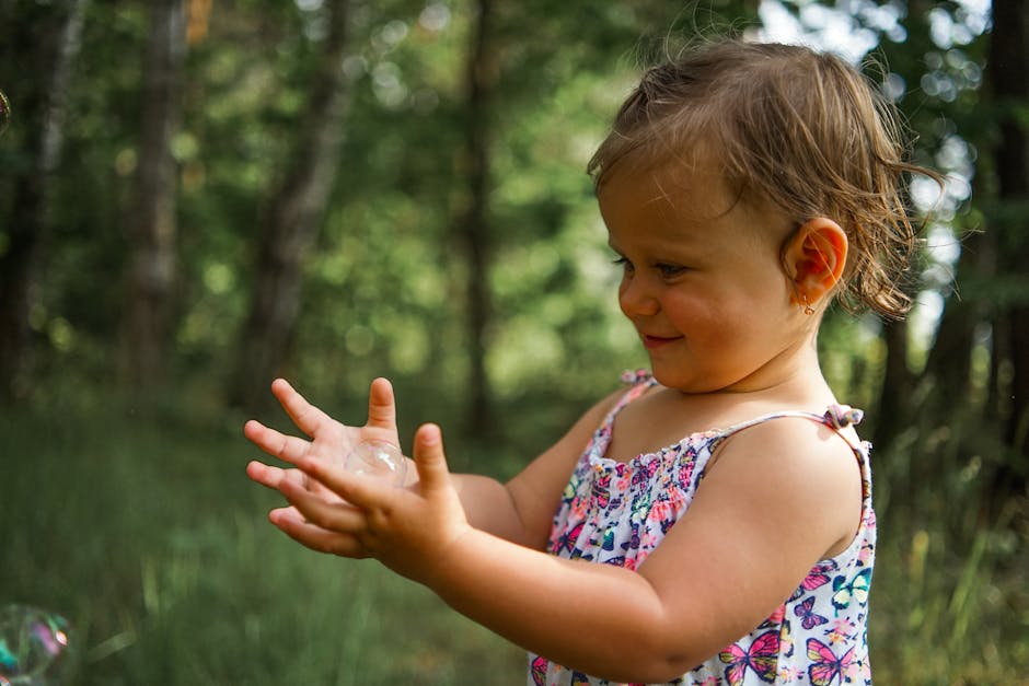 A smiling toddler plays with soap bubbles in a sunny forest setting, capturing the essence of childhood joy.