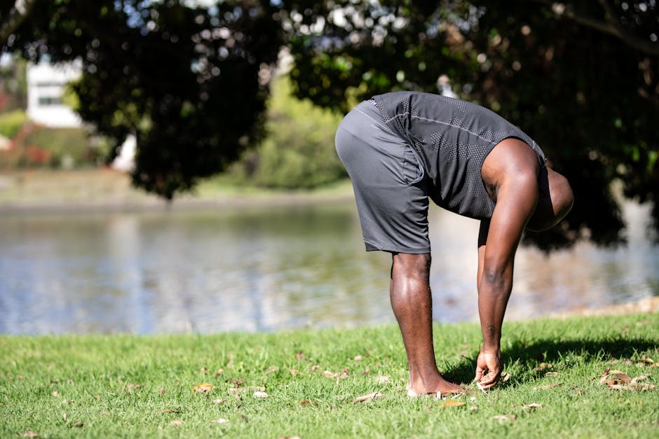 Athletic man in a park stretching near a lake during summer. Promotes fitness and relaxation.