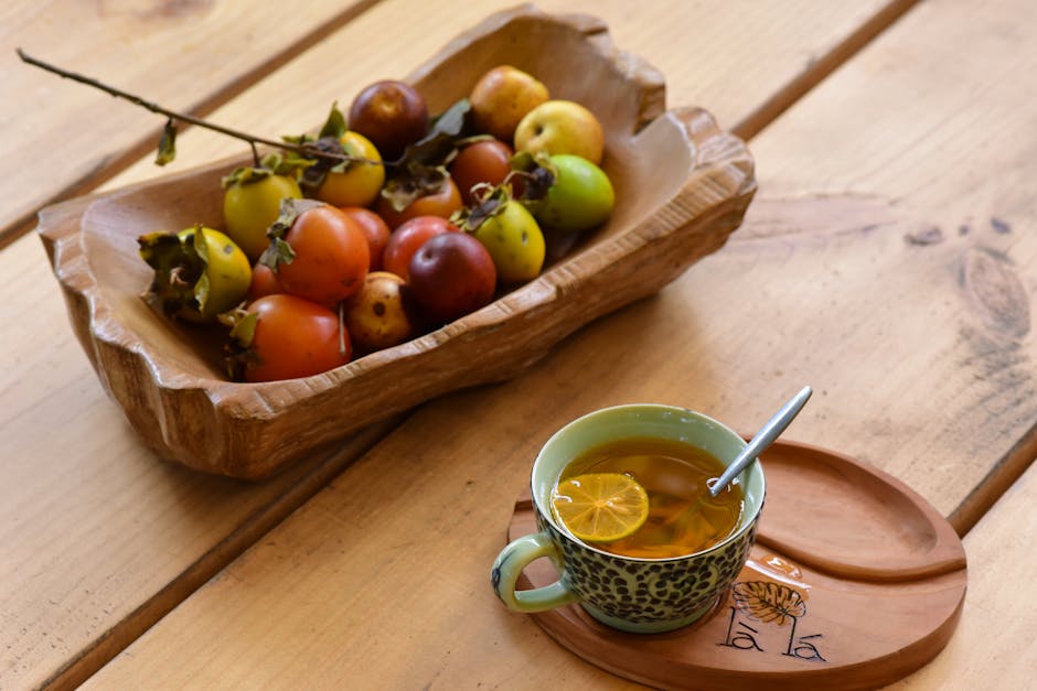 Colorful persimmons in a wooden bowl alongside a hot cup of lemon tea on a rustic table.