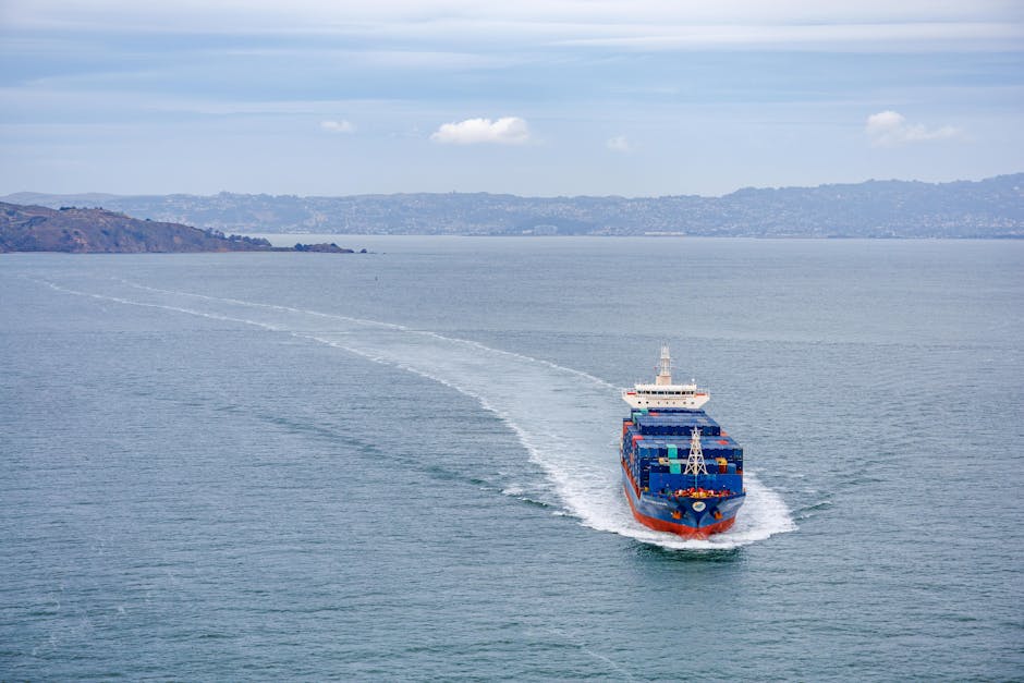 A cargo ship filled with containers travels across calm ocean waters on a clear day.