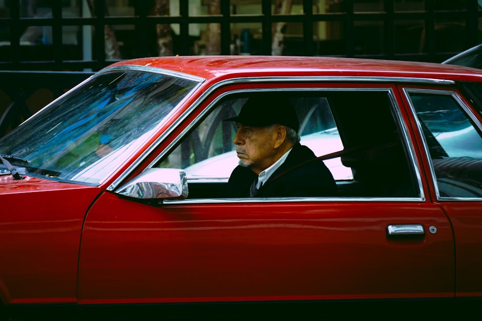Elderly man driving a vintage red car through the streets of Callao, Lima.