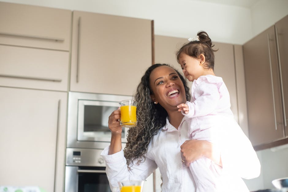 Joyful mother and child bonding in kitchen, holding glass of orange juice, expressing happiness.