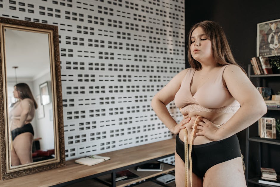 A young woman embracing body positivity while measuring her waist indoors.