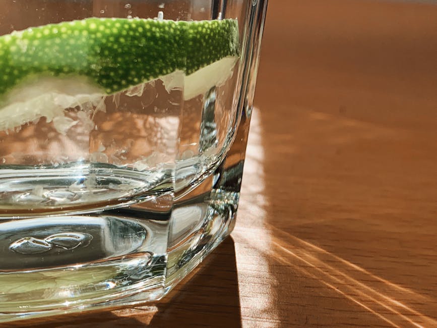 Close-up of a glass of water with a lime wedge on a sunny surface.