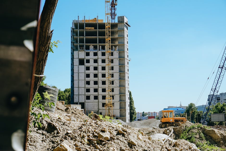 Mid-rise building under construction with cranes and machinery in a cityscape.