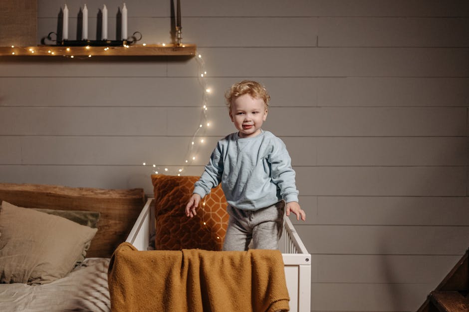 A cute baby standing in a crib with cozy decor and fairy lights in a bedroom.