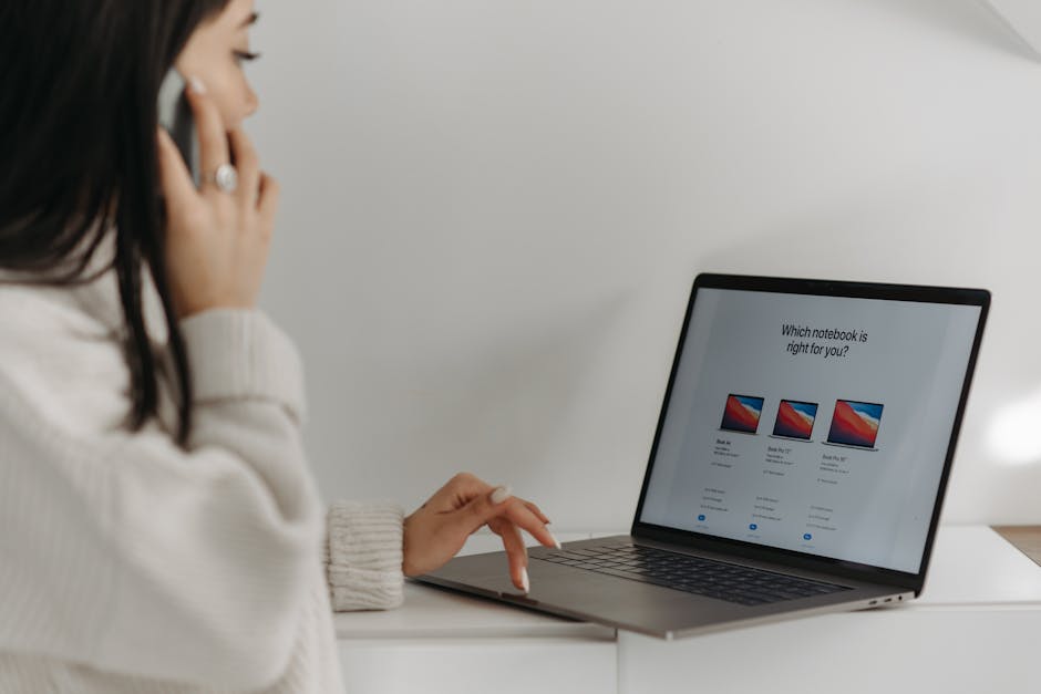 Asian woman on phone using laptop for online shopping against a white wall.