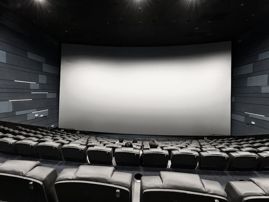 Spacious empty movie theater with a few people seated and a large blank screen.