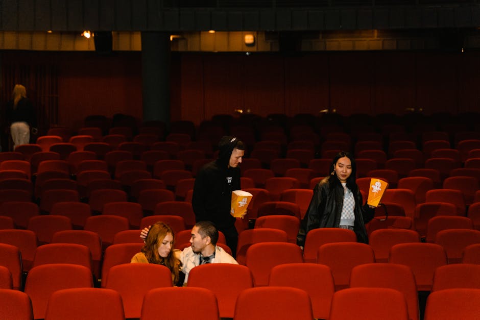 A small group of friends enjoys a movie in a cozy theater filled with red chairs.