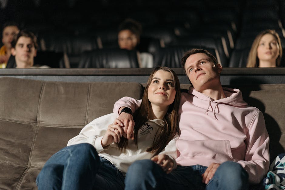 A happy couple sits closely in a theater enjoying a movie together.