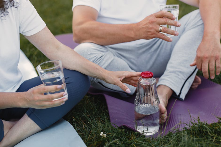 A couple relaxing outdoors on yoga mats, holding glasses of water, promoting hydration and wellness.