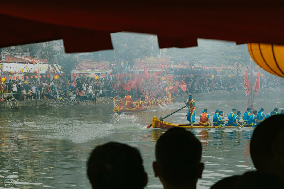 Lively dragon boat race with colorful teams and a cheering crowd by the riverbank.