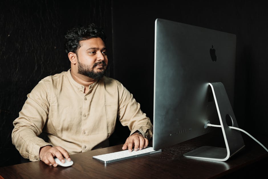Man in formal attire working at a computer in a dimly lit office setting.
